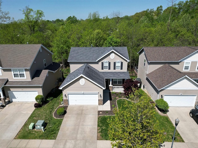 traditional home featuring a view of trees, roof with shingles, covered porch, and concrete driveway