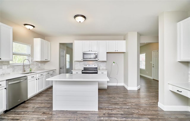 kitchen featuring backsplash, appliances with stainless steel finishes, a sink, baseboards, and white cabinetry
