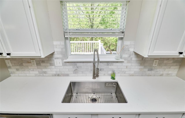 room details featuring a sink, light countertops, decorative backsplash, and white cabinetry