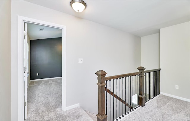 hall with baseboards, carpet, and an upstairs landing