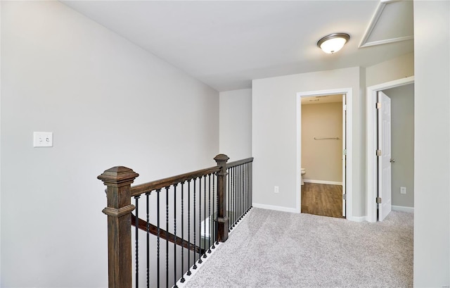 hall featuring carpet flooring, baseboards, and an upstairs landing