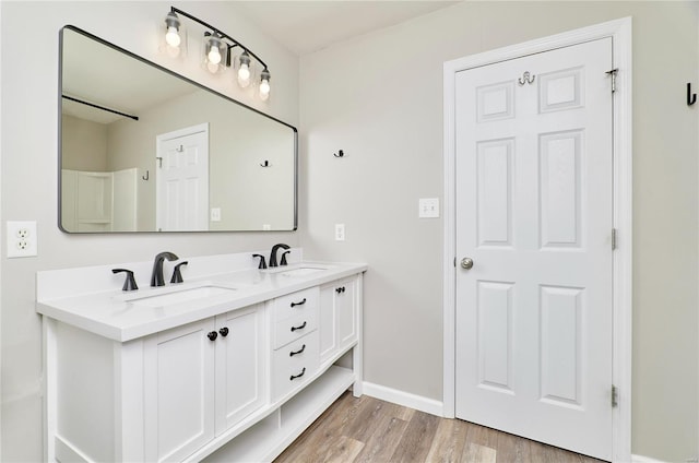 full bathroom with double vanity, baseboards, a sink, and wood finished floors