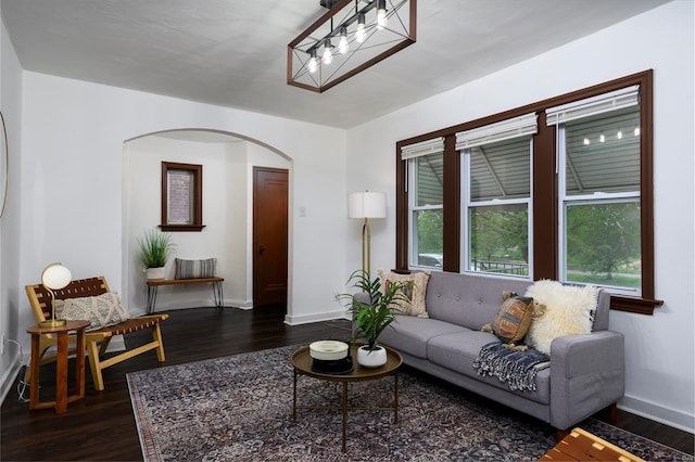 living area with arched walkways, baseboards, and dark wood-type flooring