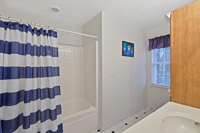 bathroom with a textured ceiling, baseboards, a sink, and shower / tub combo