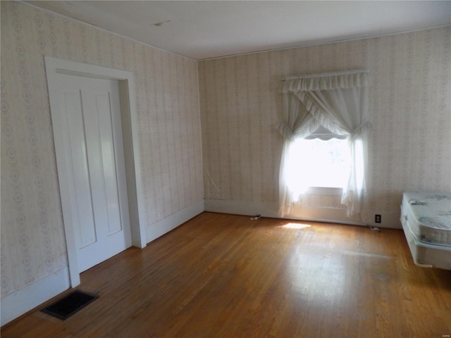 empty room featuring wallpapered walls, wood finished floors, and visible vents