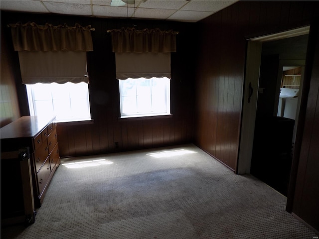 empty room with carpet floors, wood walls, and a paneled ceiling