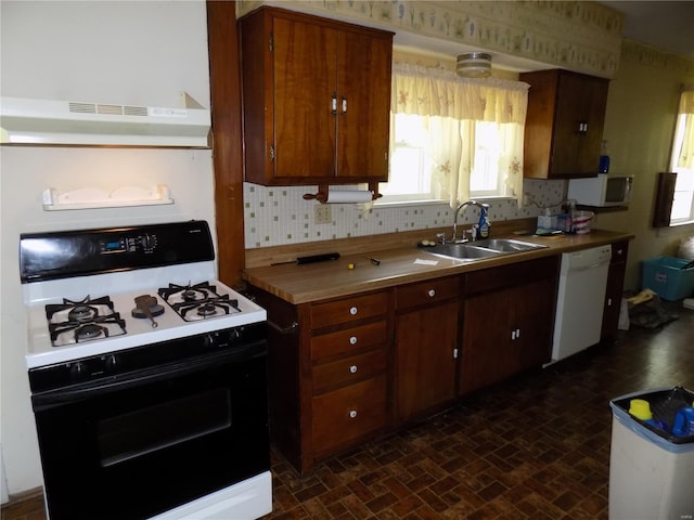 kitchen featuring white dishwasher, a sink, gas stove, backsplash, and under cabinet range hood