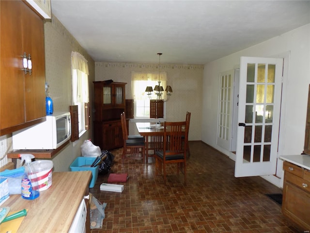 dining room featuring a notable chandelier, brick patterned floor, and wallpapered walls