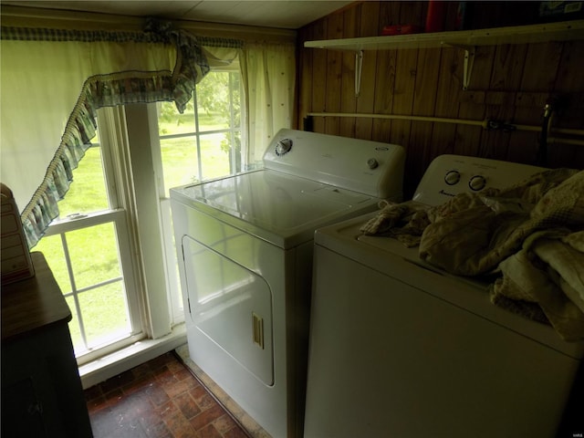 laundry area with plenty of natural light, brick floor, wooden walls, and washing machine and clothes dryer
