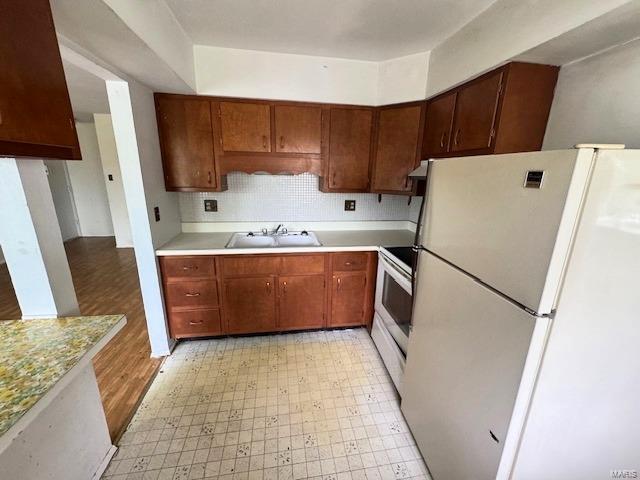 kitchen featuring a sink, white appliances, light countertops, light floors, and backsplash