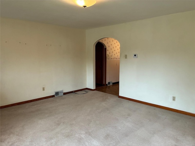carpeted spare room featuring arched walkways, baseboards, and visible vents