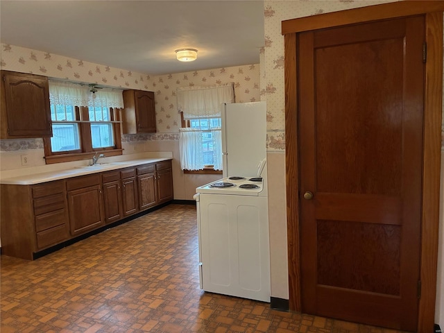 kitchen with light countertops, wallpapered walls, white electric stove, and a sink
