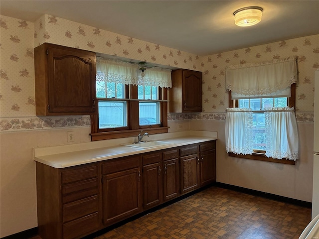 kitchen with a sink, wainscoting, and wallpapered walls