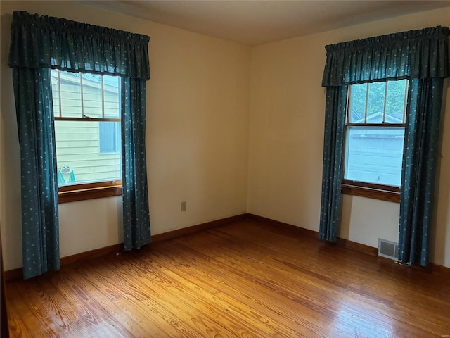 unfurnished room featuring baseboards, visible vents, a wealth of natural light, and wood finished floors