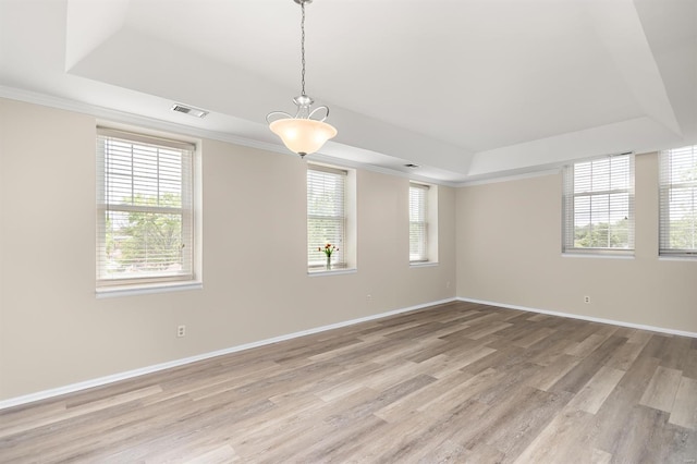 empty room with visible vents, plenty of natural light, light wood finished floors, and a raised ceiling