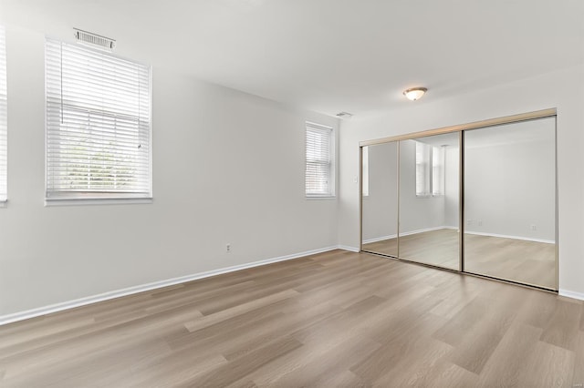 unfurnished bedroom with visible vents, baseboards, wood finished floors, and multiple windows