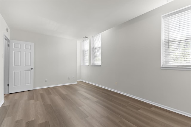 spare room featuring baseboards, wood finished floors, and a wealth of natural light