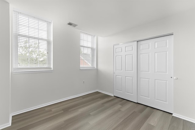 unfurnished bedroom featuring baseboards, a closet, wood finished floors, and visible vents