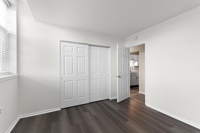 unfurnished bedroom featuring baseboards, dark wood finished floors, a sink, and a closet