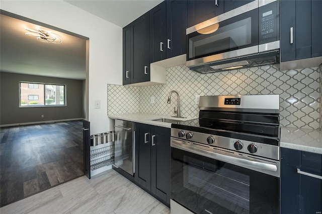 kitchen featuring light stone countertops, blue cabinets, tasteful backsplash, a sink, and stainless steel appliances