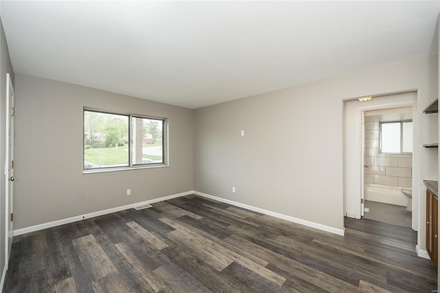 spare room featuring baseboards, dark wood-style flooring, and visible vents