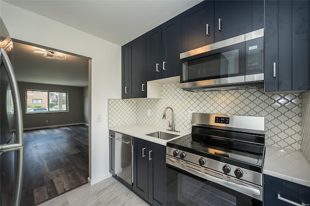 kitchen featuring decorative backsplash, appliances with stainless steel finishes, a sink, baseboards, and dark cabinetry