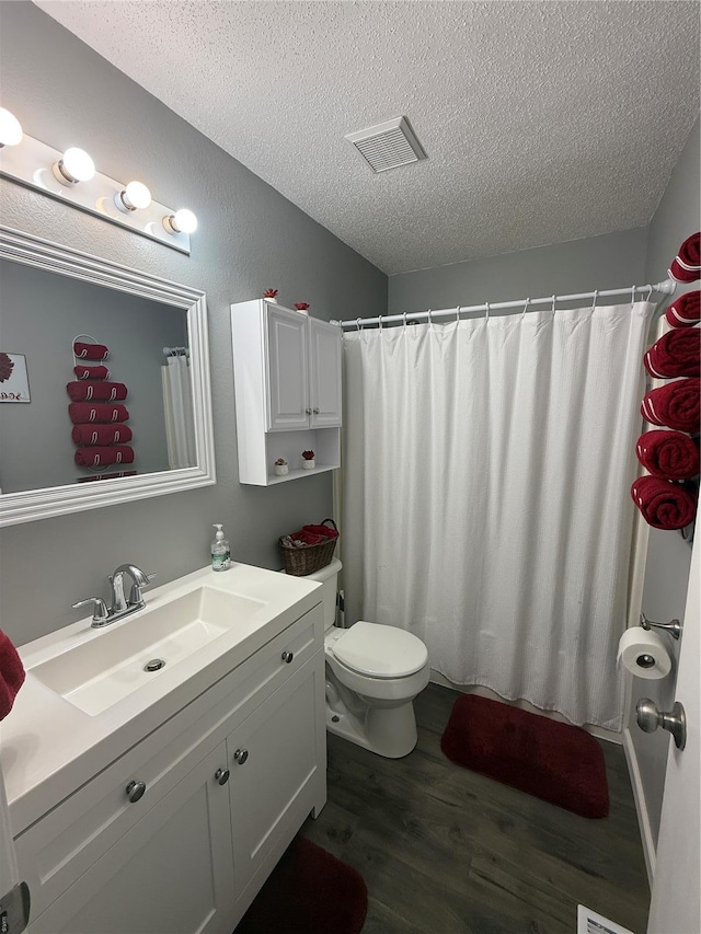 full bath with vanity, toilet, a textured ceiling, wood finished floors, and visible vents