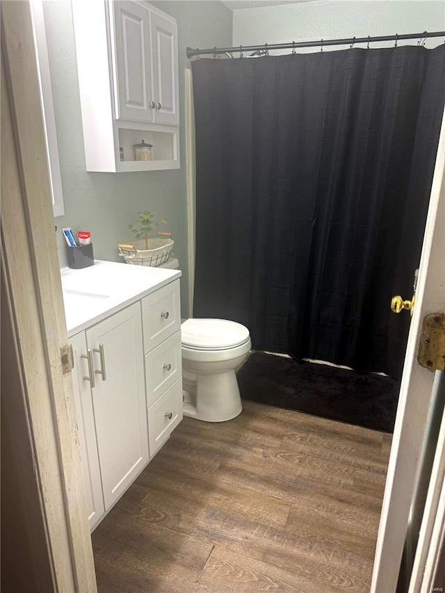 bathroom with a shower with shower curtain, toilet, wood finished floors, and vanity