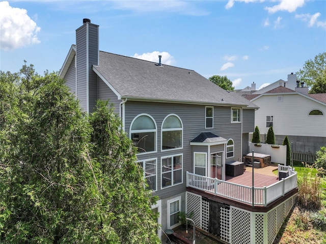 rear view of property with a shingled roof, a wooden deck, and a chimney