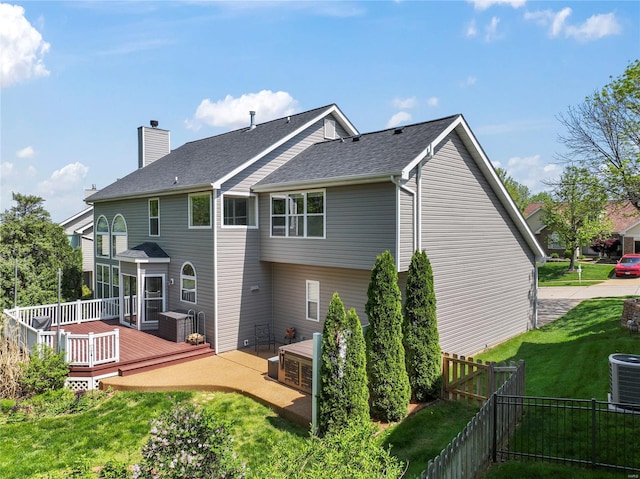 rear view of property featuring a chimney, a deck, central AC, a fenced backyard, and a yard
