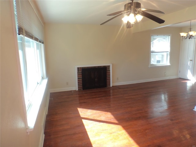 unfurnished living room with baseboards, ceiling fan with notable chandelier, a brick fireplace, and wood finished floors