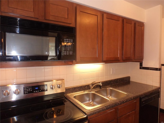 kitchen with brown cabinetry, a sink, black appliances, and dark countertops