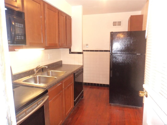 kitchen featuring dark wood-style flooring, dark countertops, a sink, visible vents, and black appliances