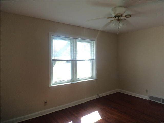 empty room featuring a healthy amount of sunlight, baseboards, dark wood finished floors, and visible vents