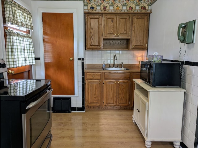 kitchen with electric range, black microwave, a sink, light wood-style floors, and brown cabinetry