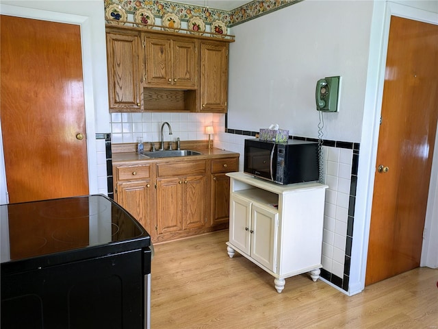 kitchen featuring brown cabinets, black microwave, a sink, light wood finished floors, and electric stove