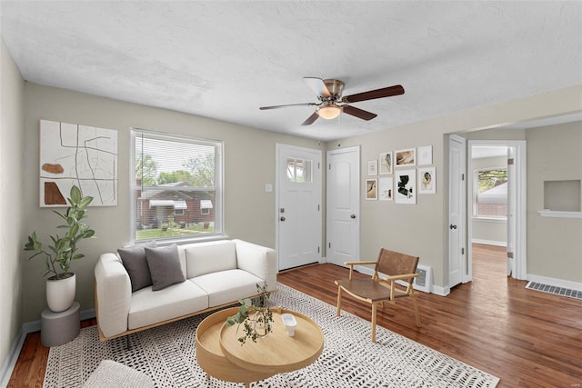 living room with ceiling fan, a textured ceiling, baseboards, wood finished floors, and visible vents