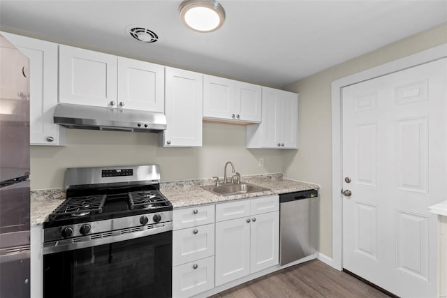 kitchen with white cabinets, appliances with stainless steel finishes, a sink, under cabinet range hood, and dark wood-style floors