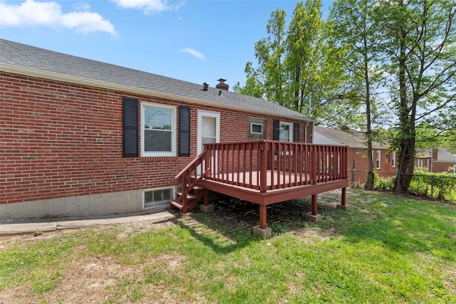 rear view of property with a chimney, a lawn, a wooden deck, brick siding, and fence