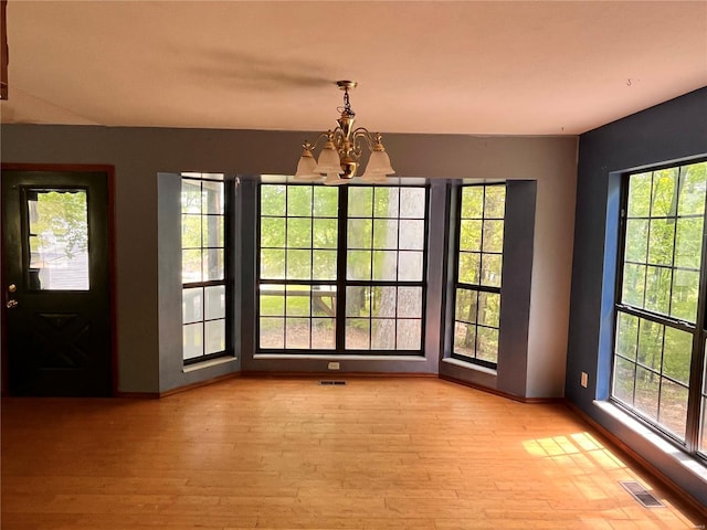 unfurnished dining area featuring visible vents, a healthy amount of sunlight, an inviting chandelier, and light wood-type flooring