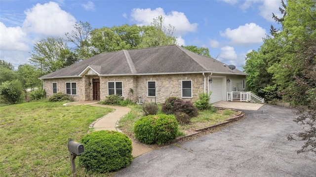 ranch-style home featuring driveway, a front yard, roof with shingles, an attached garage, and stone siding