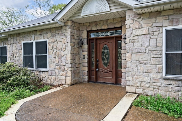entrance to property featuring a shingled roof and stone siding