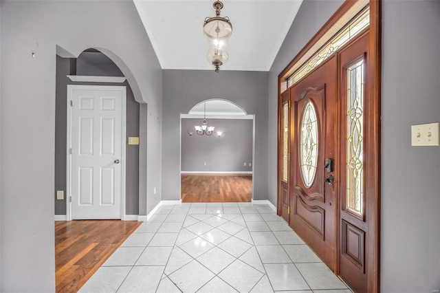 entrance foyer featuring arched walkways, a chandelier, baseboards, light tile patterned floors, and ornamental molding