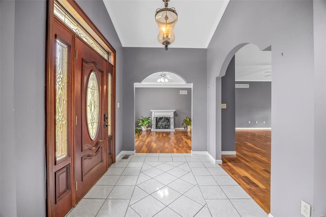 entrance foyer with ornamental molding, a fireplace with raised hearth, arched walkways, a ceiling fan, and light tile patterned floors