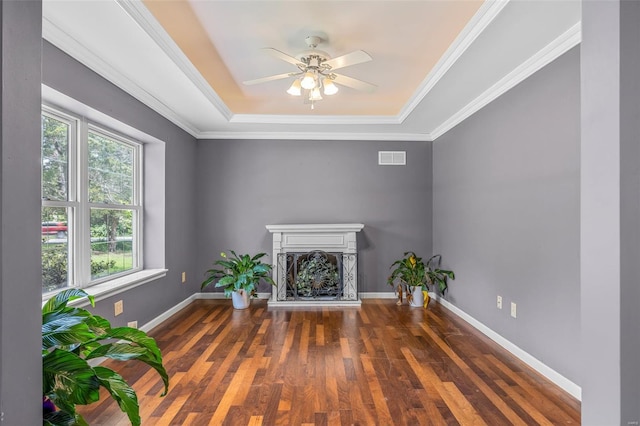unfurnished living room with a fireplace with raised hearth, a ceiling fan, wood finished floors, a tray ceiling, and visible vents