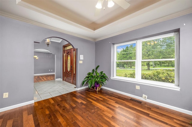 unfurnished room with arched walkways, ceiling fan, wood finished floors, and a tray ceiling