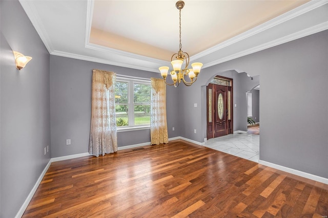 unfurnished dining area featuring ornamental molding, wood finished floors, baseboards, a chandelier, and arched walkways