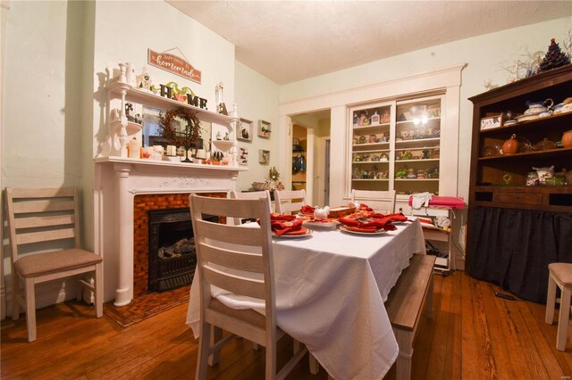 dining space featuring a brick fireplace, a textured ceiling, and hardwood / wood-style flooring