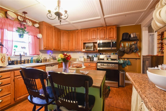 kitchen featuring an inviting chandelier, light wood-type flooring, brown cabinets, a sink, and appliances with stainless steel finishes