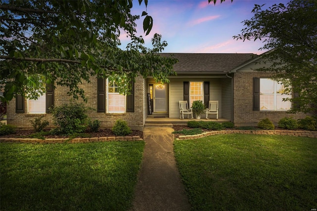 ranch-style house featuring a yard, roof with shingles, brick siding, and covered porch